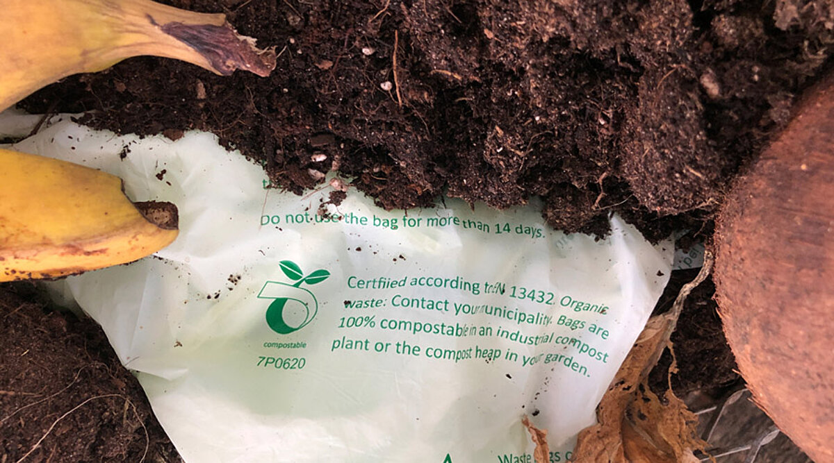 Ein kompostierbarer Beutel liegt in einem Komposthaufen