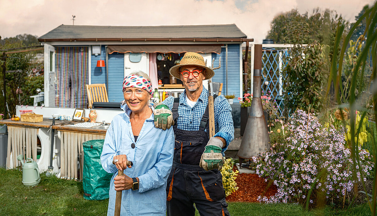 Garden owner couple stands with garden tools in front of their garden shed in the countryside