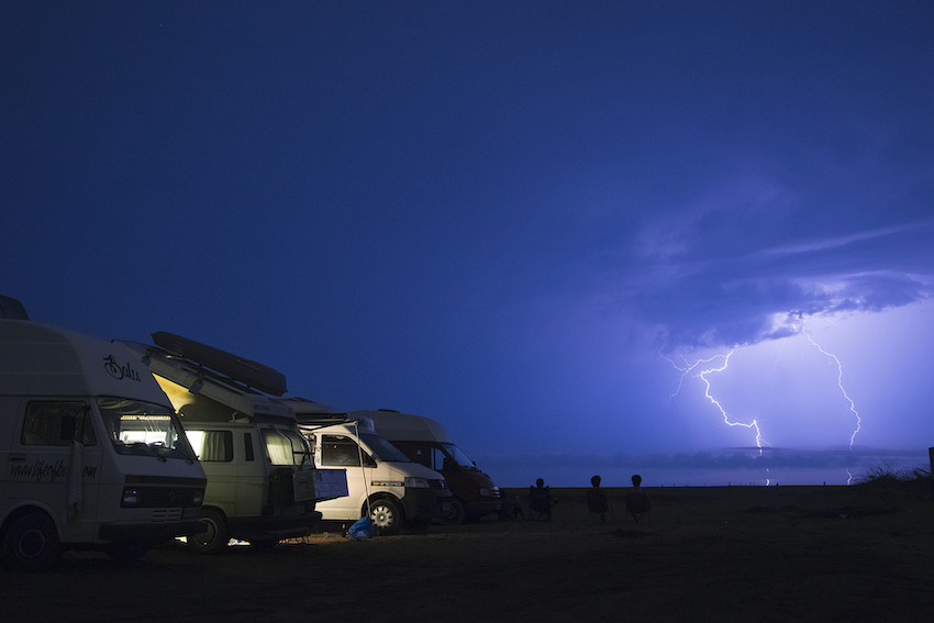 Vier Campervans auf einer Wiese, im Hintergrund ein Blitz.