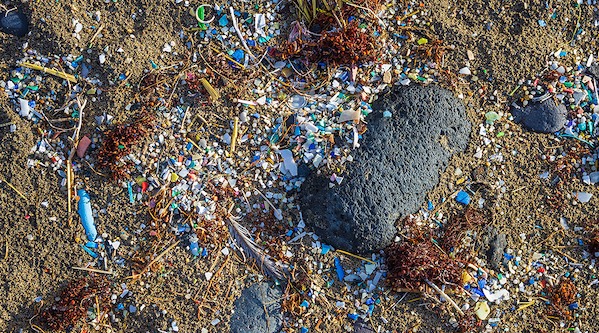 Ein Sandstrand mit kleinen und großen angespülten Plastikteilen. 
