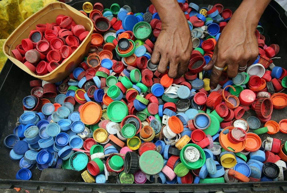 Frau sortiert farbige Flaschendeckel um sie danach recyclen zu können.