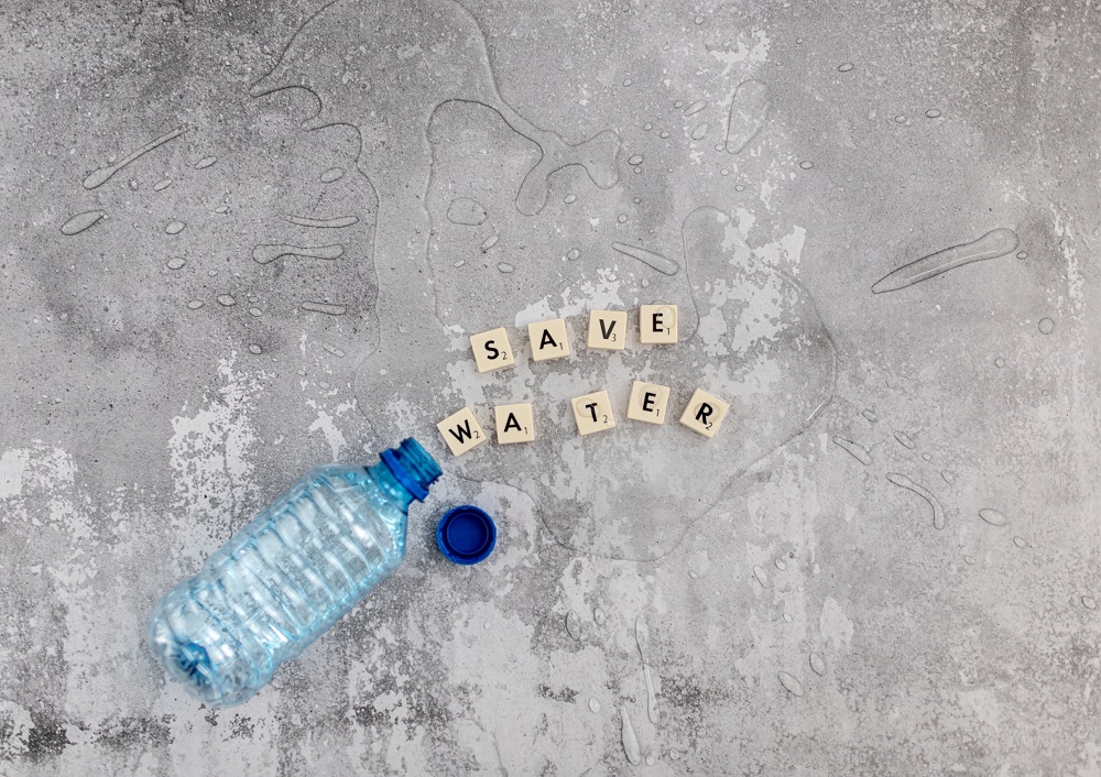 Eine umgekippte Plastikflasche liegt auf einem Betonboden und Scrabble-Buchstaben buchstabieren die Worte 